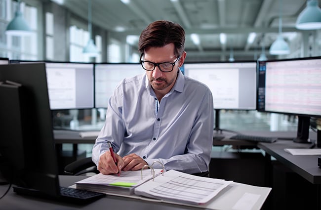 Man working on papers surrounded by computers